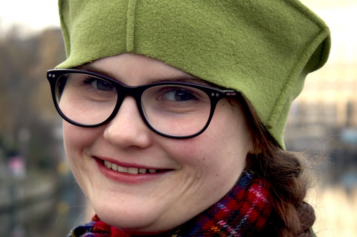 Vinie Walling smiling into the camera and wearing a green hat and tartan scarf