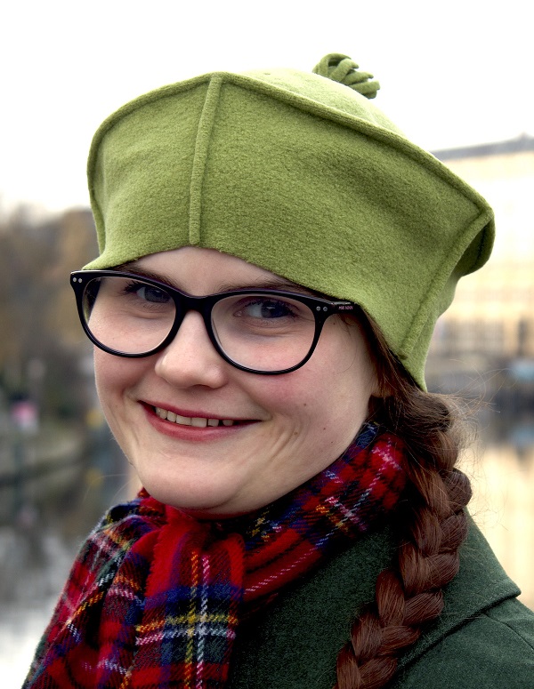Vinie Walling smiling into the camera and wearing a green hat and coat with a tartan scarf